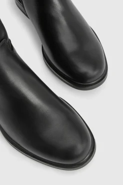Bottes plates montantes jusqu'aux genoux aux détails de ferrures imposantes