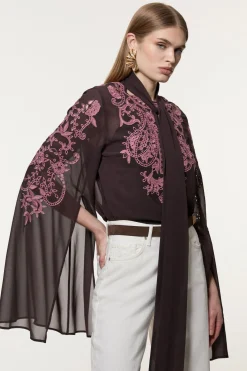 Chemisier long tissé en georgette aux découpes ajourées et orné de perles, avec un col noué et des manches dramatiques.